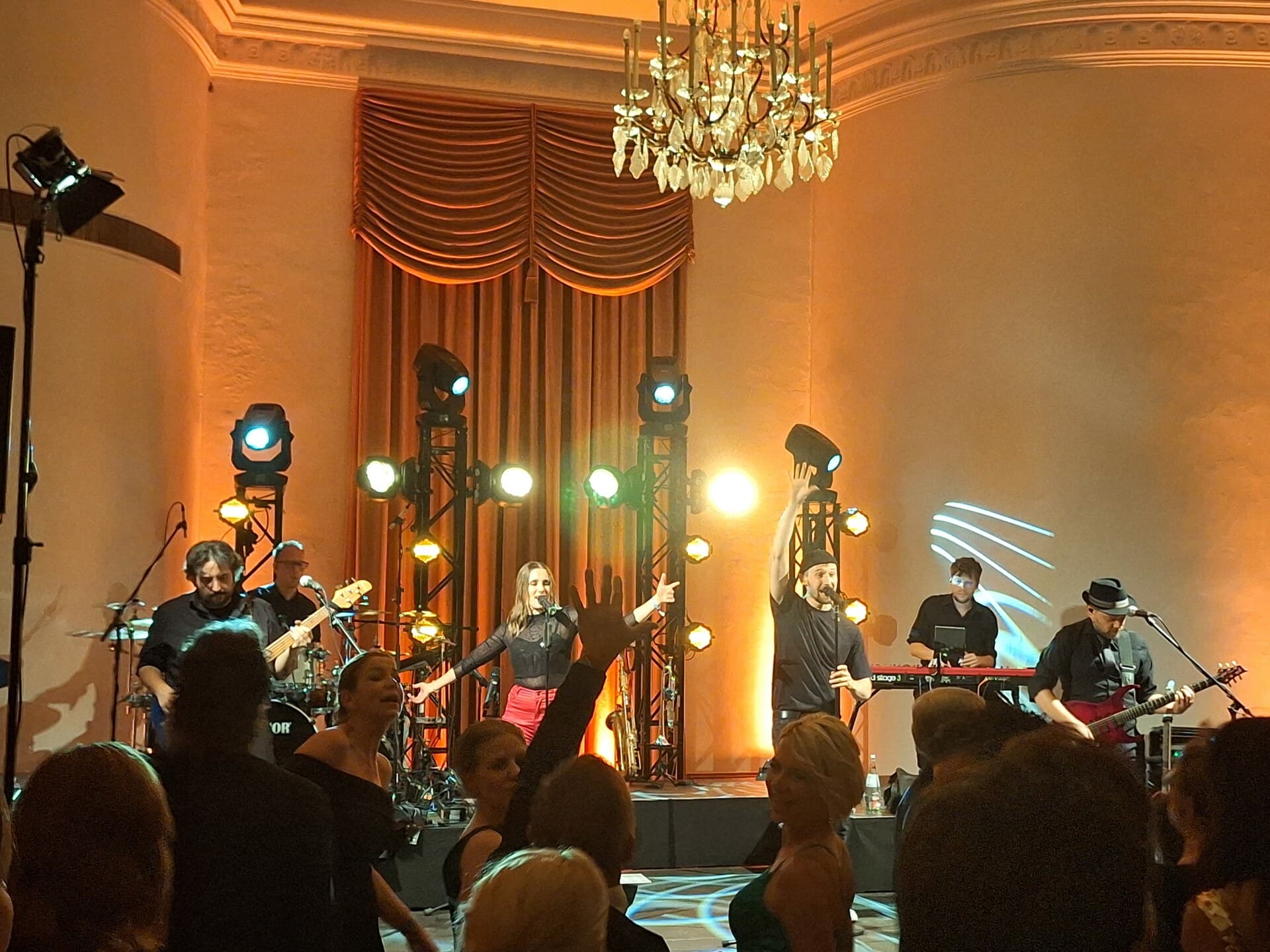 Band im warm beleuchteten Festsaal mit Publikum vor der Bühne