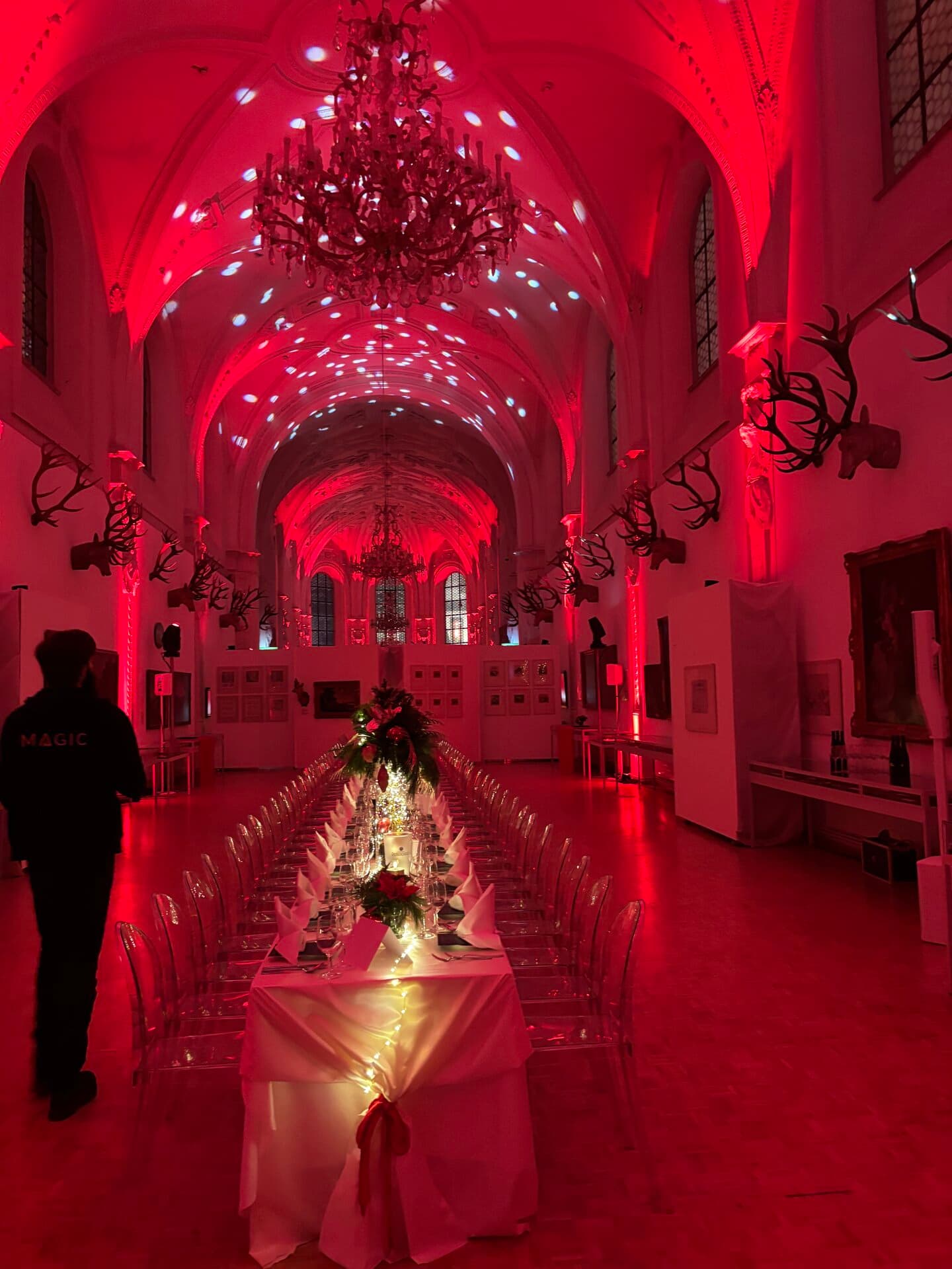 Festsaal in rotem Licht mit festlich gedeckter Weihnachtstafel unter Kronleuchtern